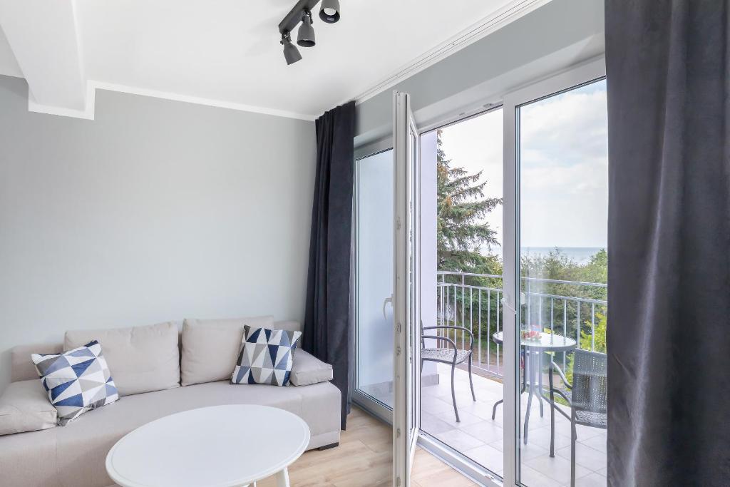 Cozy sofa by open glass doors leading to small balcony with chairs and tree view