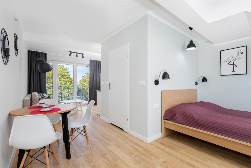 Studio interior showing bed with plum cover, dining table, floor lamp, and balcony doors
