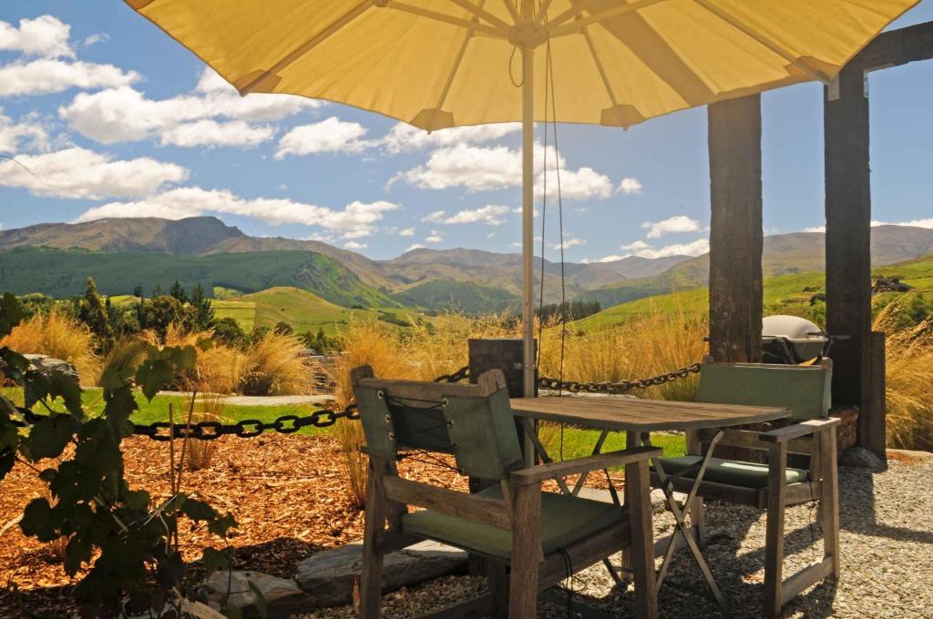 a table and chairs with an umbrella and mountains at HawkRidge Alpine Suite in Queenstown