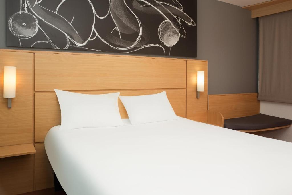 ein Schlafzimmer mit einem großen weißen Bett und einem Gemälde in der Unterkunft ibis 3 Lacs Neuchâtel in Thielle