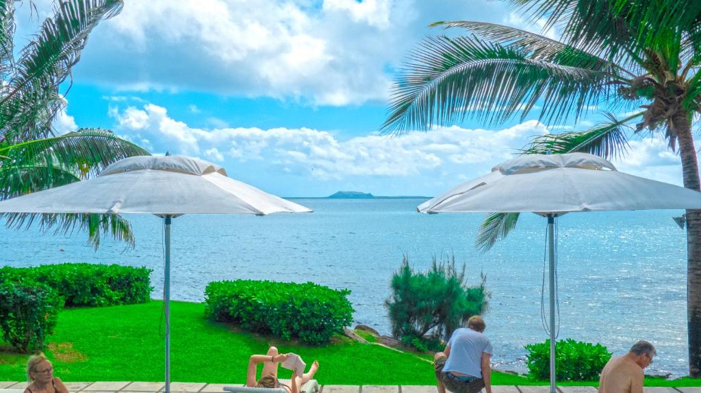 un gruppo di persone seduti sotto gli ombrelloni vicino all'oceano di Myra Luxury Seafront Apartment a Cap Malheureux