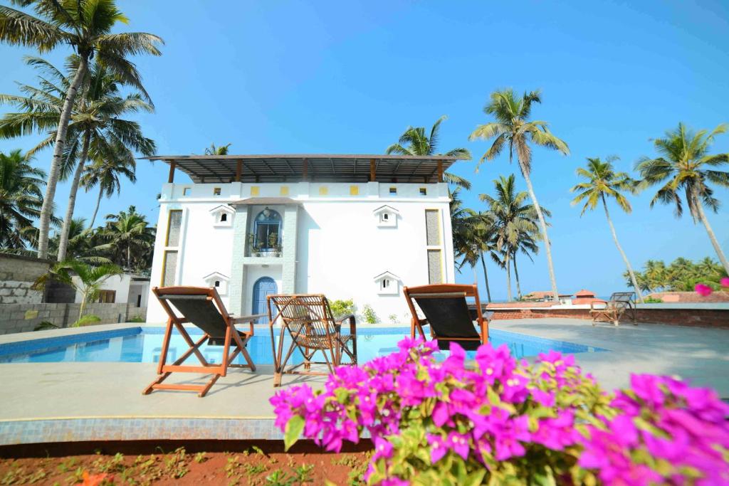 a villa with a swimming pool and two chairs and flowers at Magnolia Guesthouse Varkala in Varkala