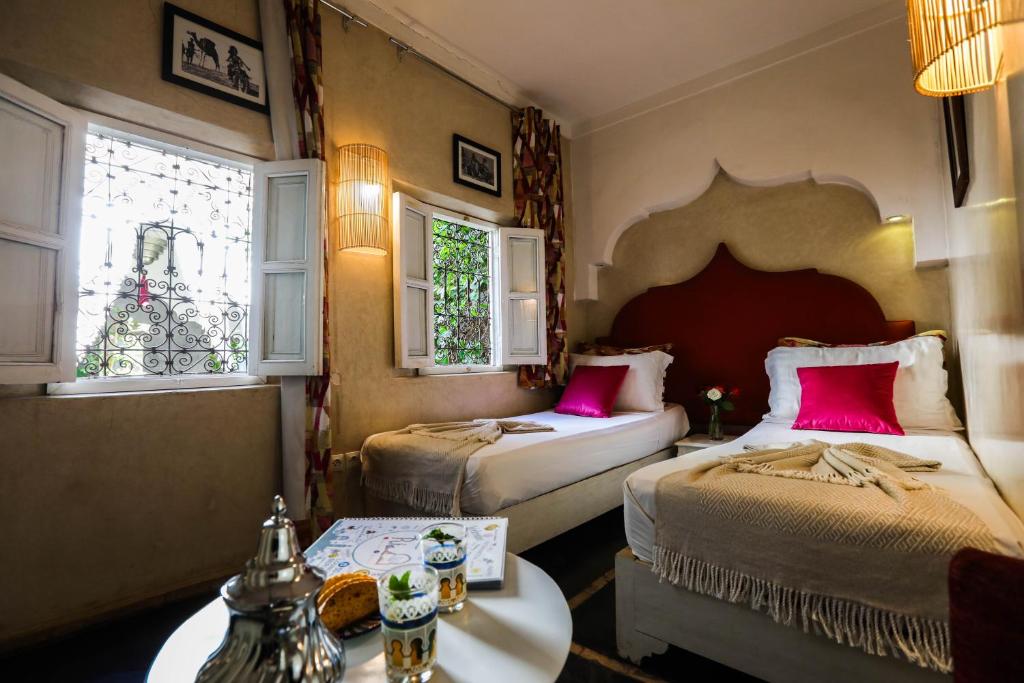 マラケシュにあるリヤド レ 2 ポルツのベッドルーム1室(ピンクの枕とテーブル付きのベッド2台付)