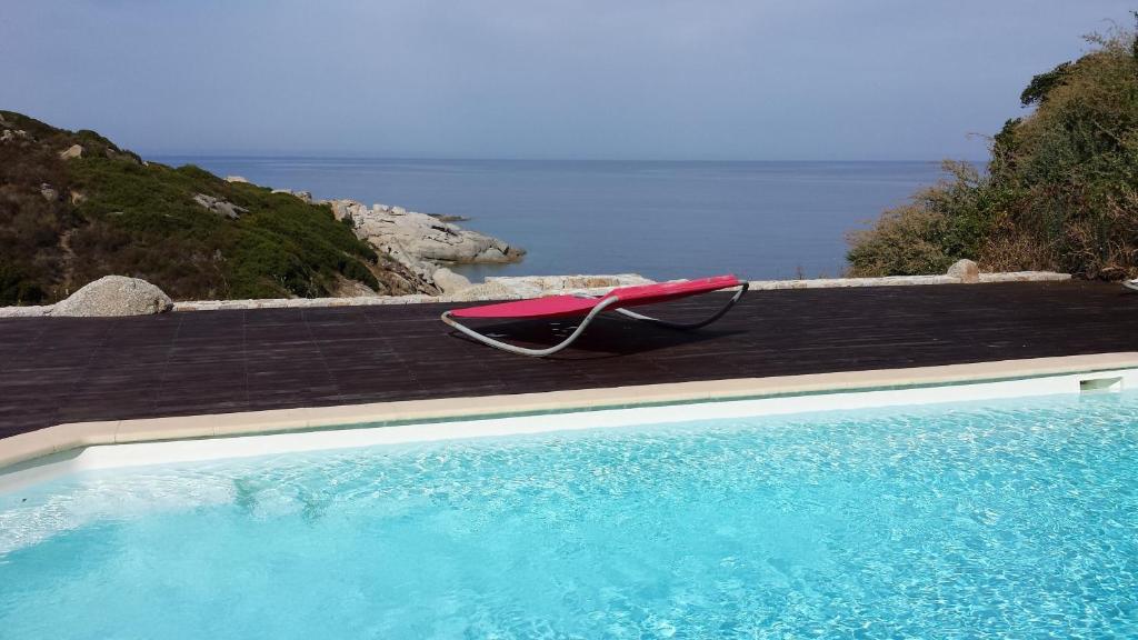 uma piscina com um guarda-sol vermelho junto ao oceano em Castelia em Lumio