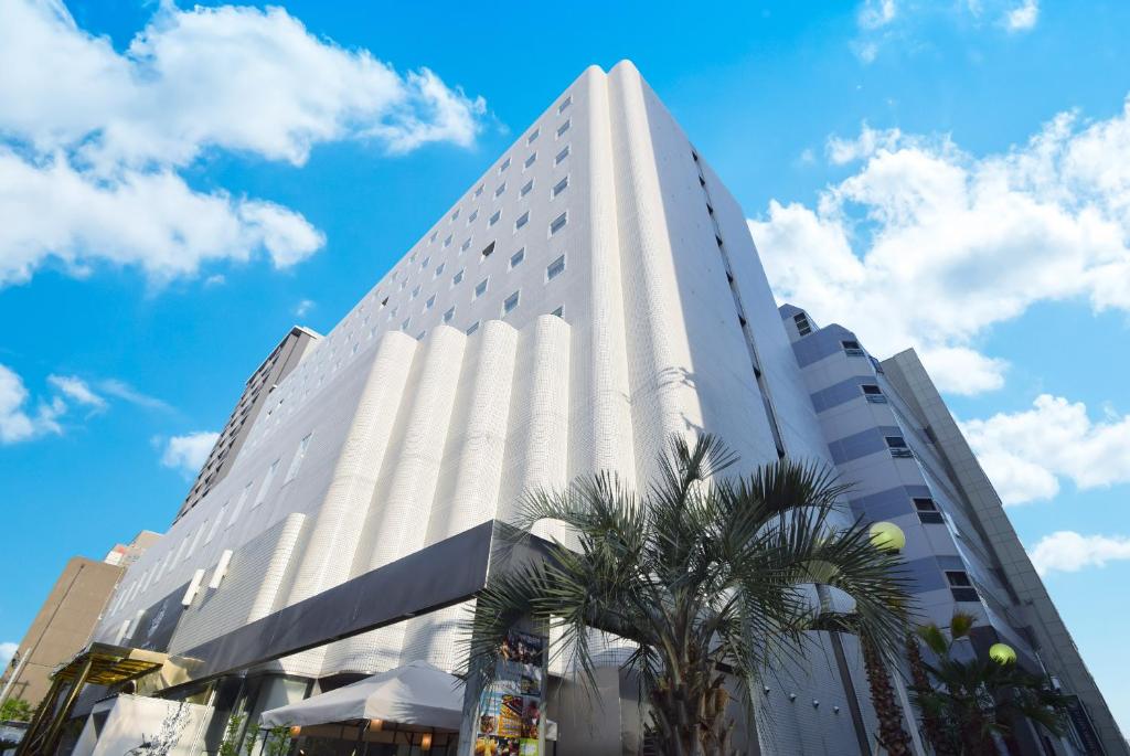 a tall white building with palm trees in front of it at IP City Hotel Osaka - Imperial Palace Group in Osaka