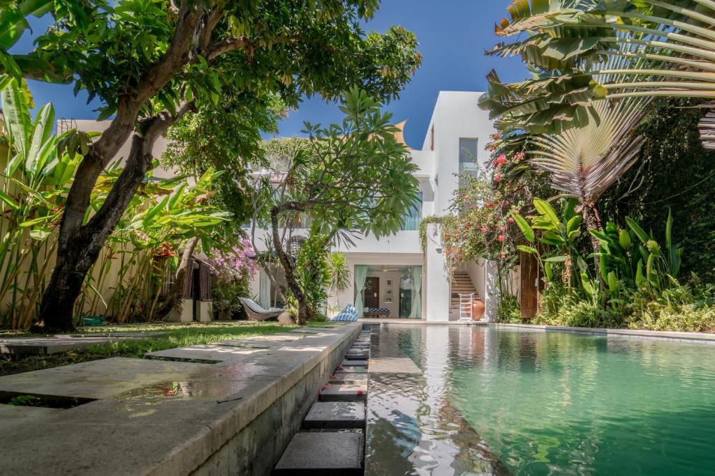 a swimming pool in front of a house with trees at Villa Saffira in Seminyak