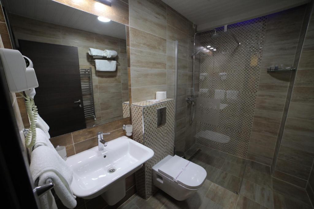 Hotel bathroom with glass-enclosed shower, wall-mounted hairdryer, towel rack, heated towel rail and sink at City Palace Hotel in Ohrid