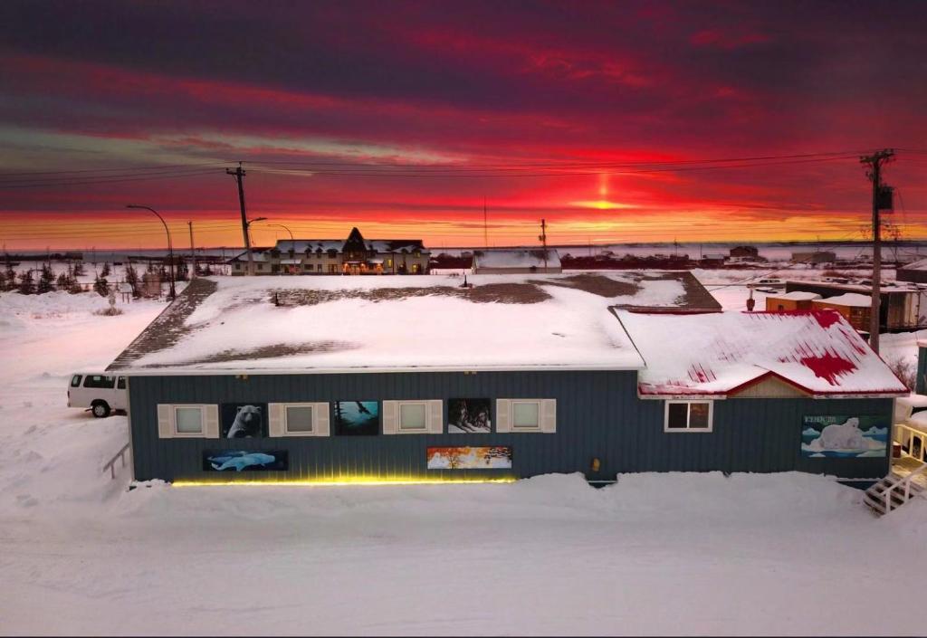 een huis bedekt met sneeuw met een zonsondergang op de achtergrond bij IceBerg Inn in Churchill
