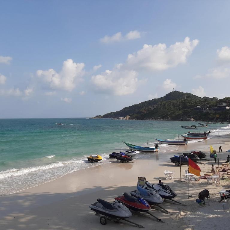 a beach with boats and chairs and the ocean at Sunrise Resort- Koh Phangan - SHA Extra Plus in Haad Rin