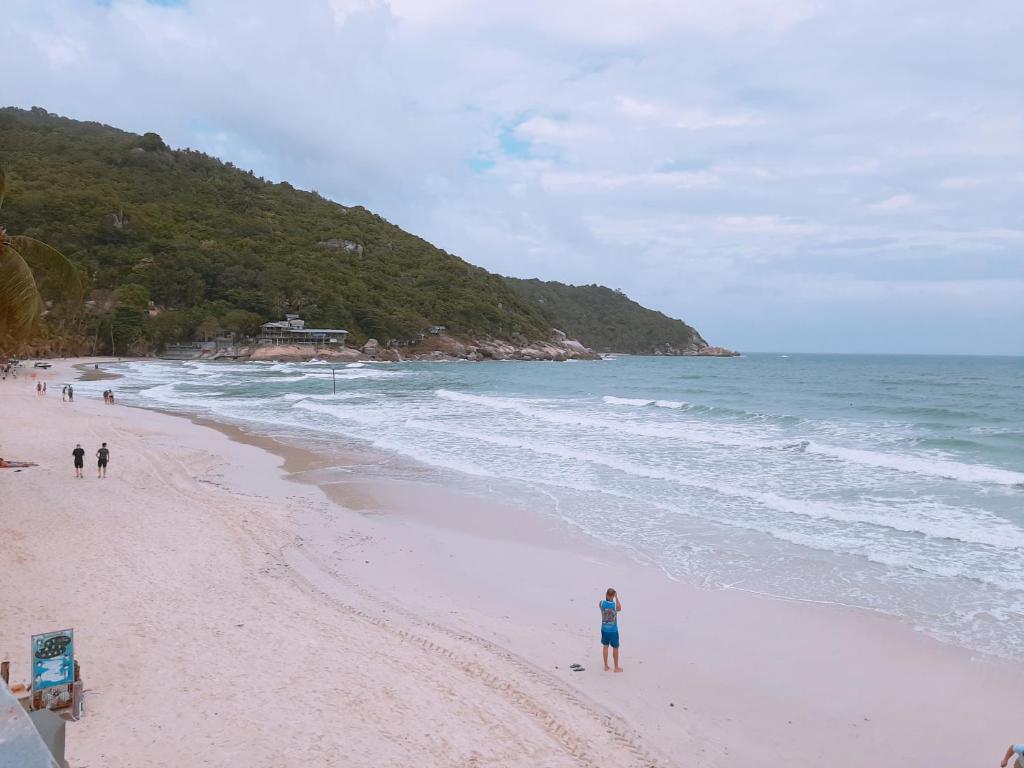 a person standing on a beach next to the ocean at Sunrise Resort- Koh Phangan - SHA Extra Plus in Haad Rin