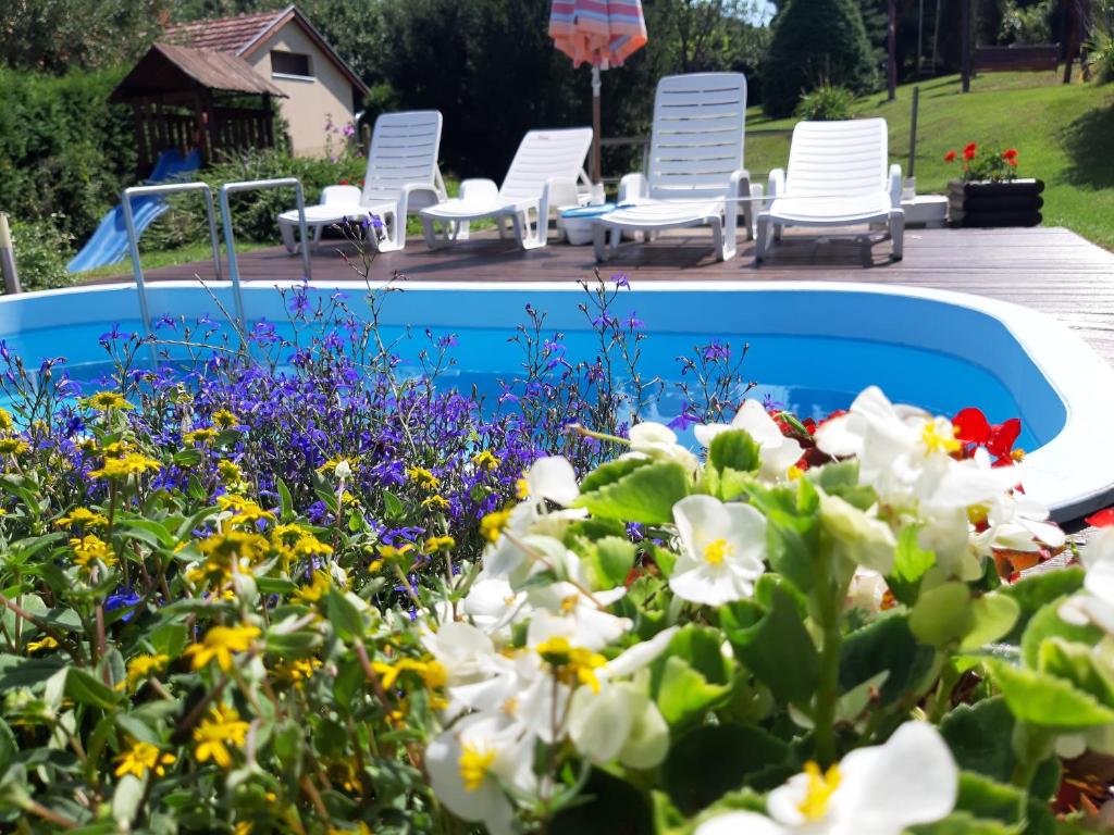 einen Garten mit weißen Stühlen und Blumen neben einem Pool in der Unterkunft Boglárka Vendégház in Vasvár