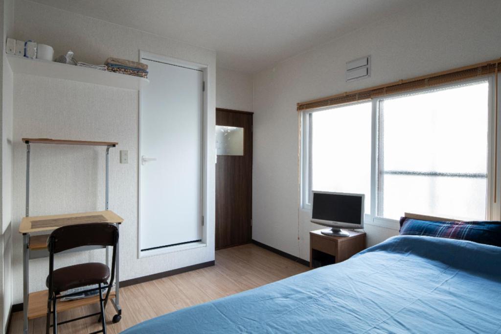 a bedroom with a bed and a desk and a television at Guesthouse Erimo Apartment in Sapporo