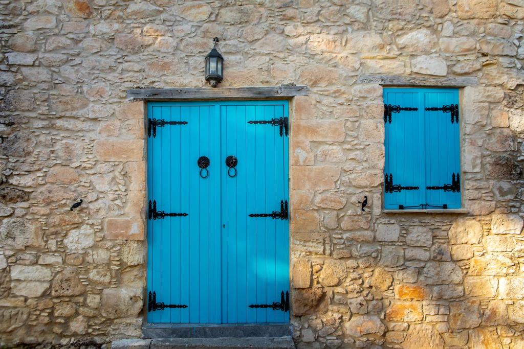 une porte bleue et deux fenêtres dans un bâtiment en pierre dans l'établissement Akamantida Platea, à Pano Arodes