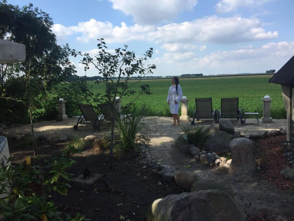 una donna in piedi in un giardino con sedie e un campo di Wellness Sauna Beauty Farm Midwolda a Midwolda