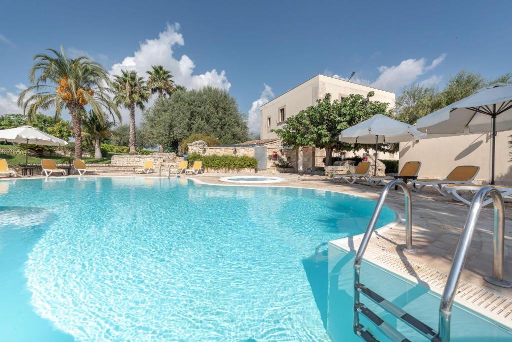 a large swimming pool with chairs and umbrellas at Relais Torre Marabino in Ispica