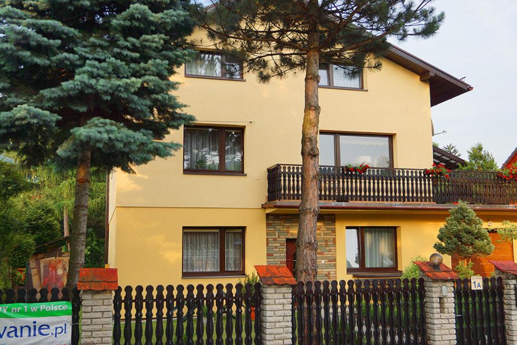 a yellow house with a black fence and trees at Apartamenty pokoje INA in Ustroń
