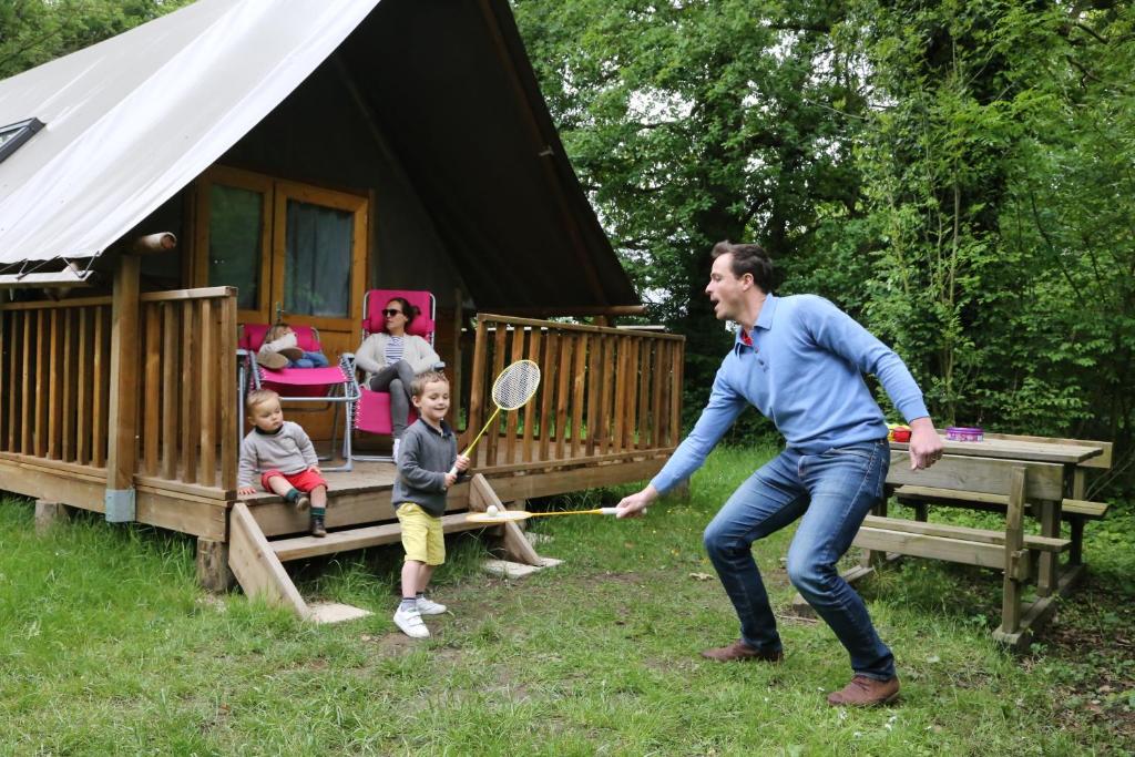 a man and two children playing with a tennis racket at Camping le Nid du Parc in Villars-les-Dombes