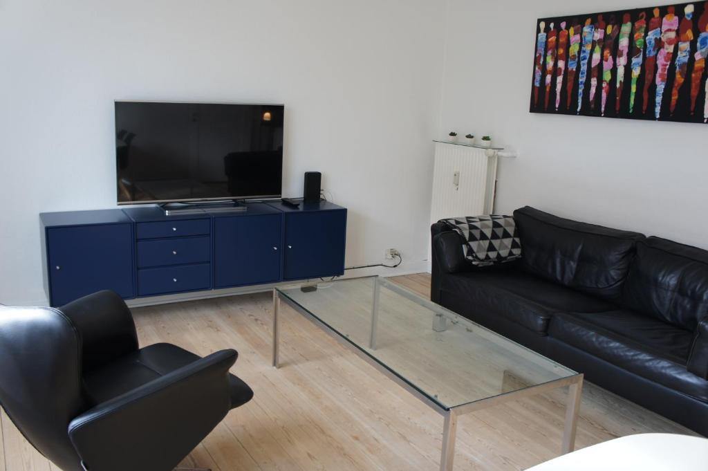 ein Wohnzimmer mit einem schwarzen Ledersofa und einem TV in der Unterkunft 90. Kronprinsensg. (190) in Esbjerg
