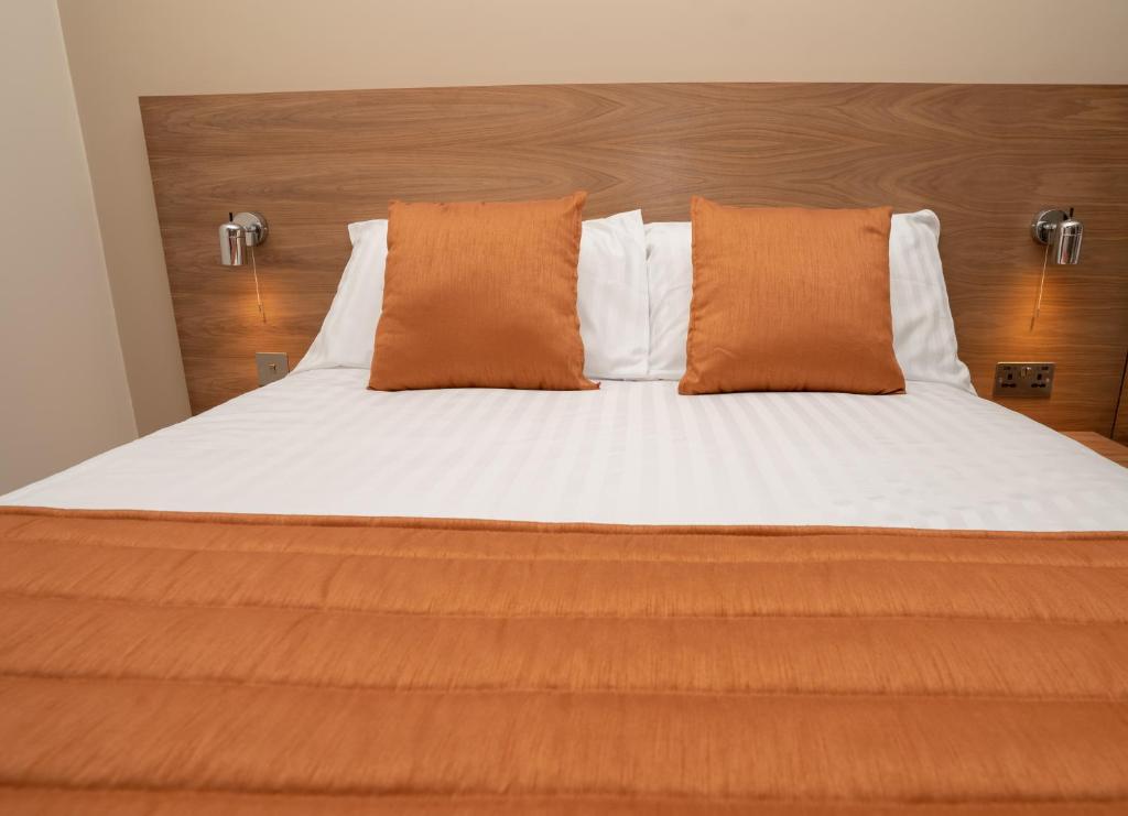 a bed with orange and white sheets and pillows at Eagle Hotel Luton Airport in Luton