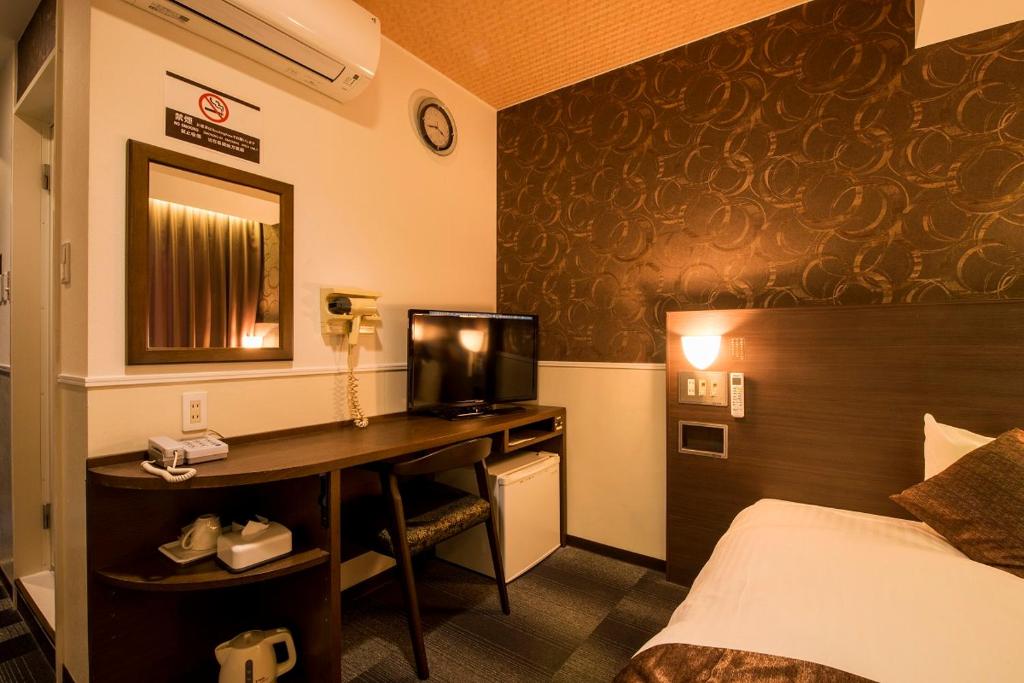 a hotel room with a bed and a desk with a television at Sejour Inn Nagarekawa in Hiroshima
