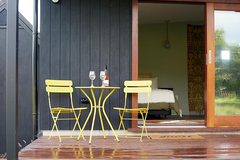 two chairs and a table with wine glasses on a porch at Studio 40 in Coromandel Town