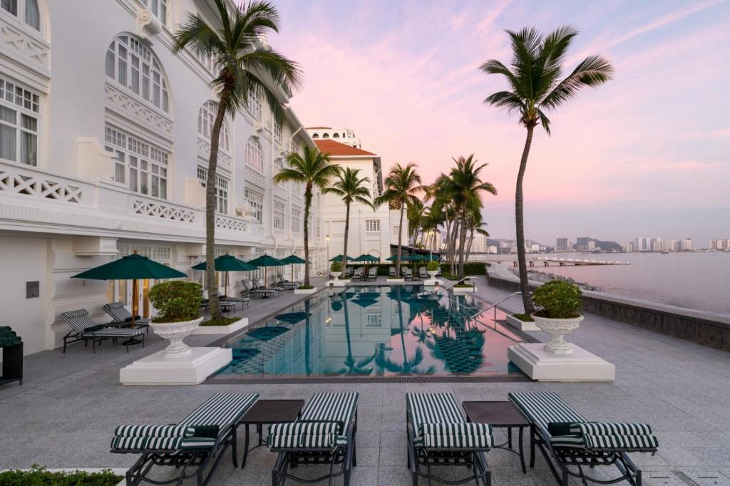 a hotel pool with palm trees and tables and chairs at Eastern & Oriental Hotel in George Town