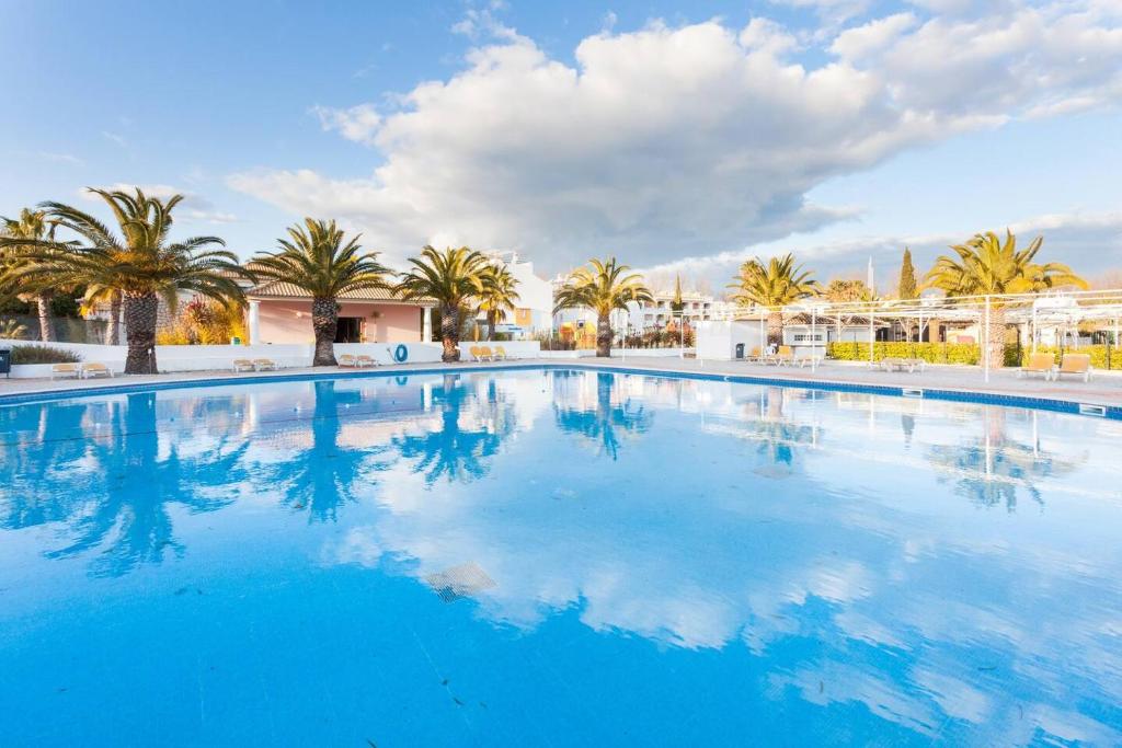 a large swimming pool with palm trees in the background at Cabanas Gold By Beach Rentals in Cabanas de Tavira
