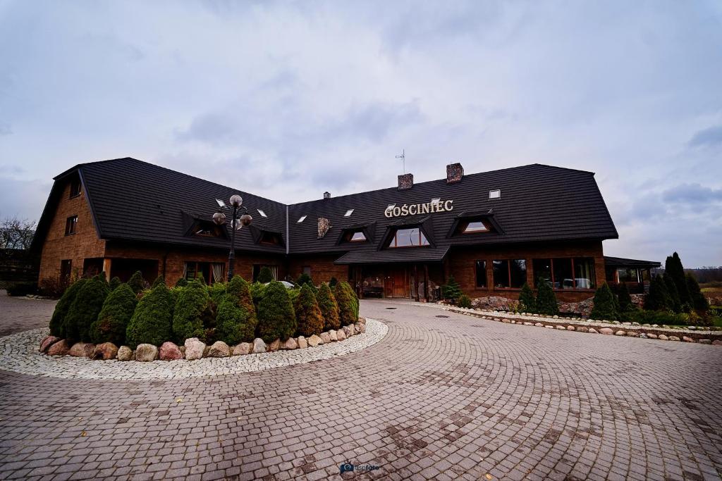 a building with a black roof on a brick road at Gościniec pod Strzechą in Suwałki