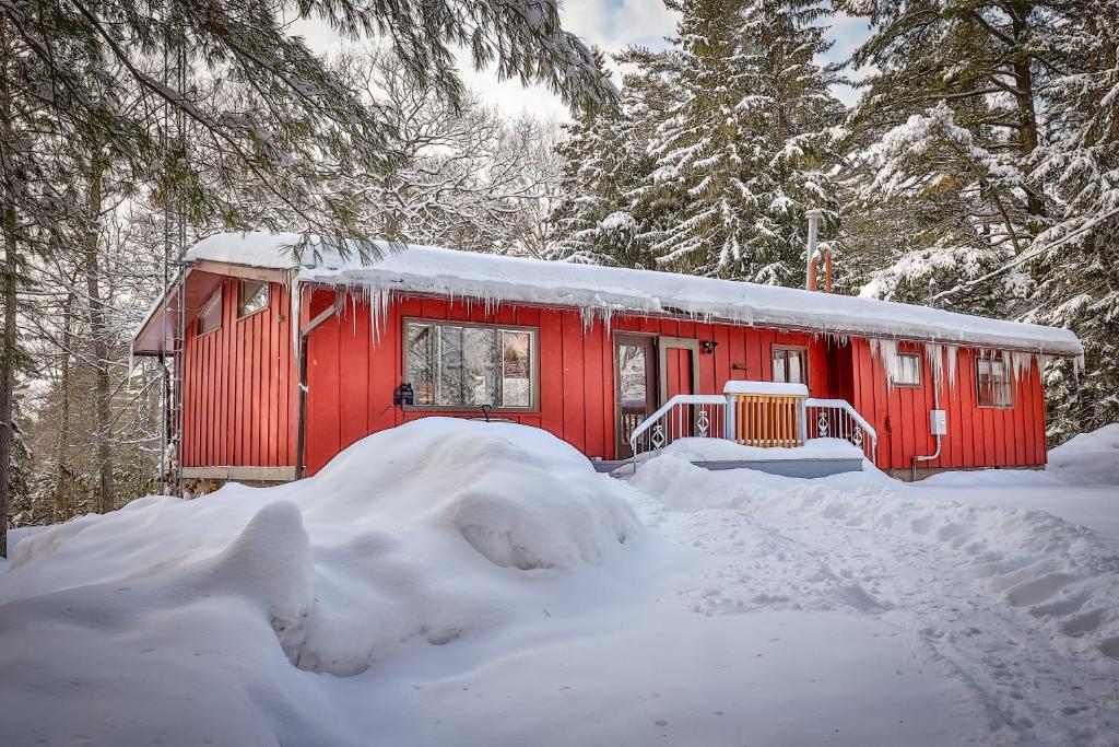 a red cabin in the snow with snow covered trees at Vance Bay Getaway in Manitowish Waters