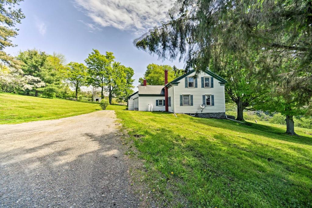 a white house on a green field with a dirt road at Stamford Farmhouse with Deck in Catskill Foothills in Stamford