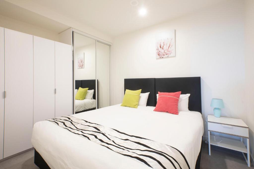 - une chambre avec un grand lit blanc et des oreillers colorés dans l'établissement Platinum City Serviced Apartments, à Melbourne