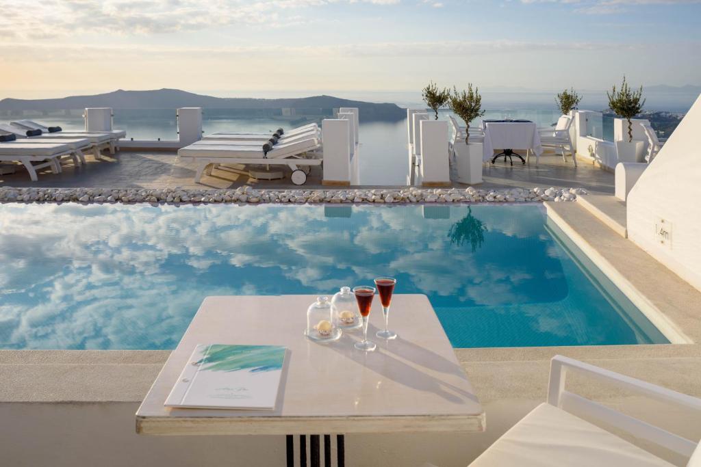 a table with wine glasses on it next to a swimming pool at Above Blue Suites in Imerovigli