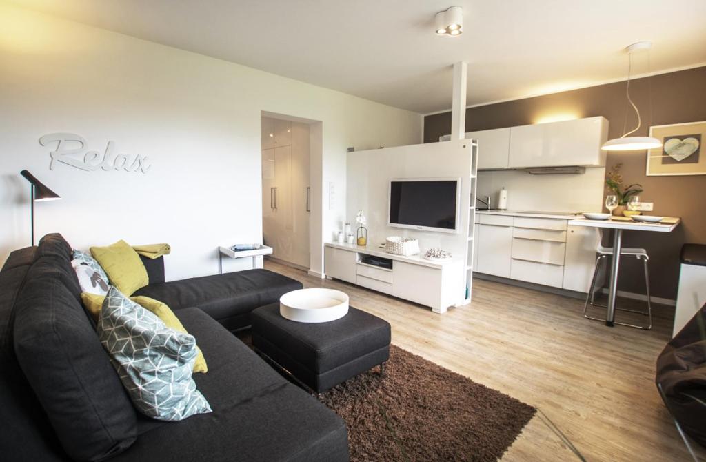 a living room with a black couch and a kitchen at Haus Dünenbake, Ferienwohnung Strandpeter Wohnung 13 in Sankt Peter-Ording