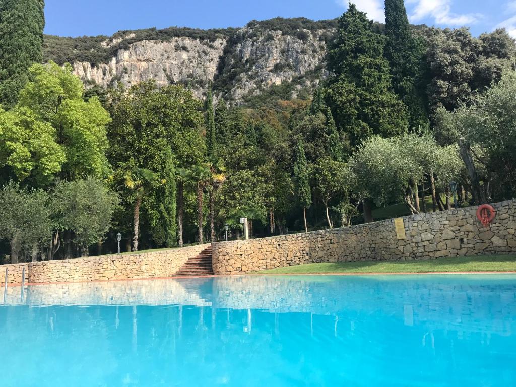 una piscina azul de agua con una pared de piedra y árboles en Parco Villa San Vigilio en Garda