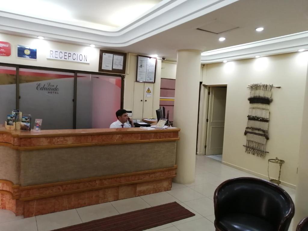 a man sitting at a reception desk in a lobby at Hotel Don Eduardo in Temuco