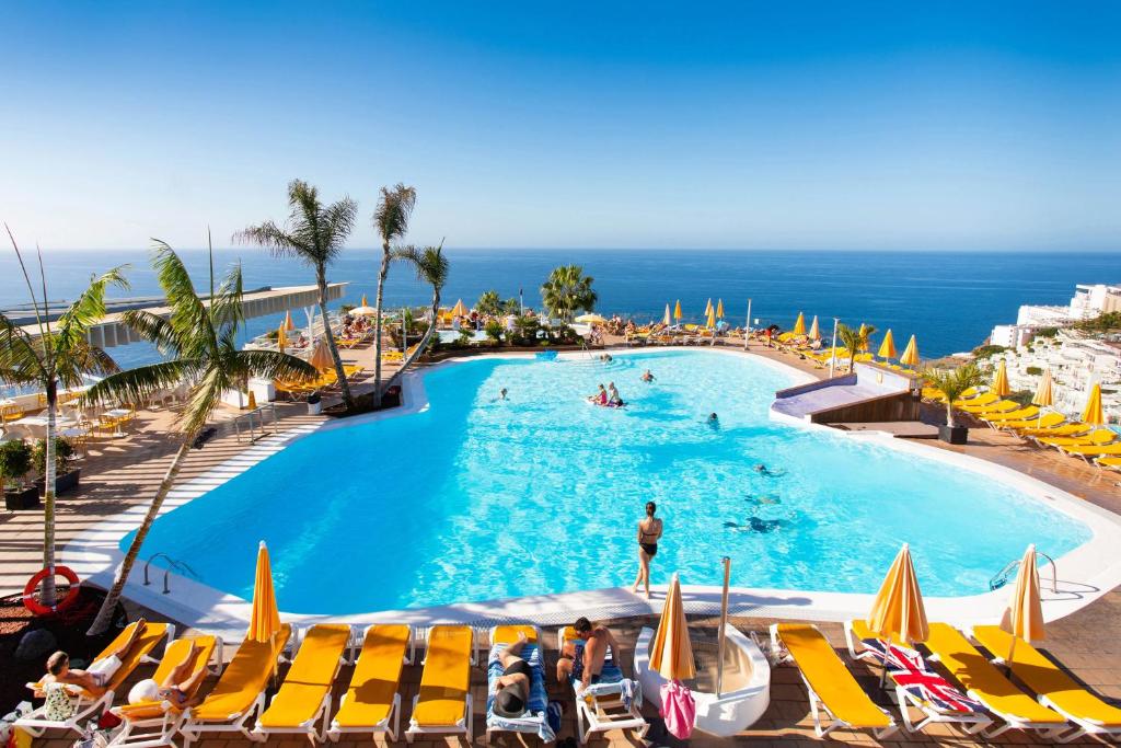 a swimming pool with chairs and the ocean in the background at Hotel Riosol in Puerto Rico de Gran Canaria