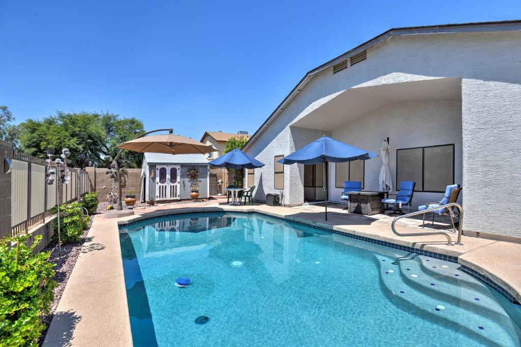 a swimming pool with chairs and umbrellas next to a house at Glendale Home with Pool - Walk to NFLandNHL Games! in Glendale