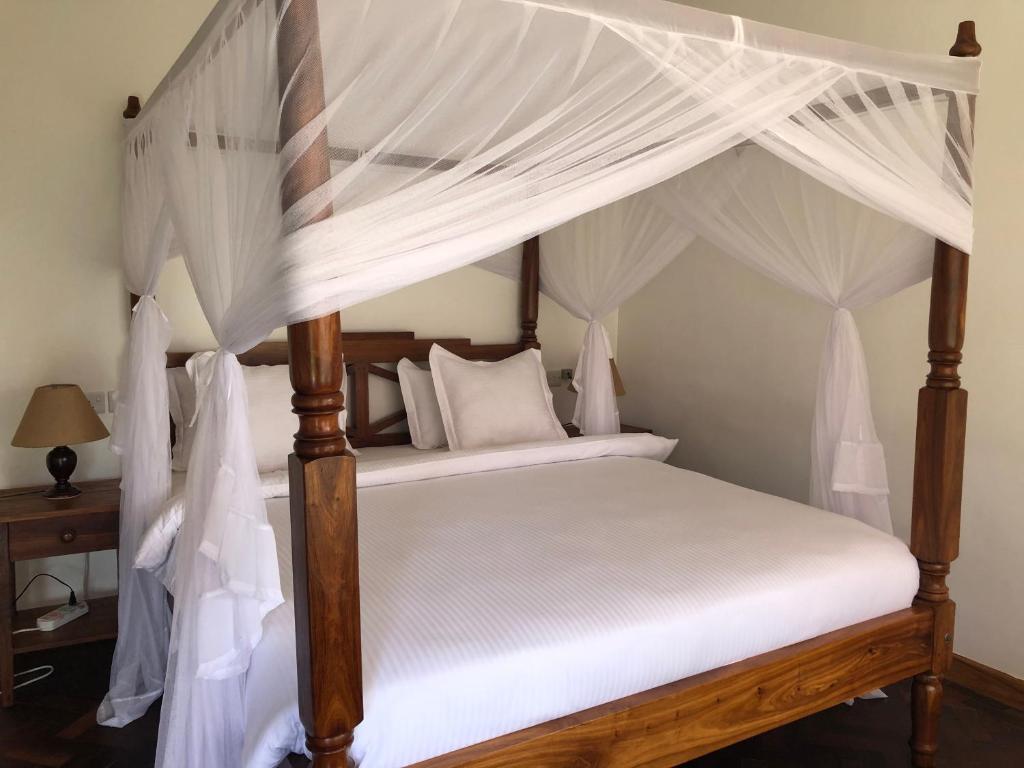 1 dormitorio con cama con dosel y cortinas blancas en Bird of Paradise Eco Lodge, en Arusha