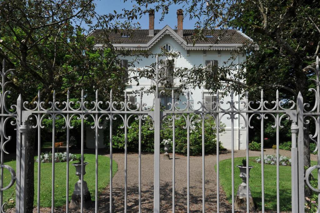 een versierde metalen hek voor een wit huis bij La Maison D'hôtes du Parc in Ronchamp