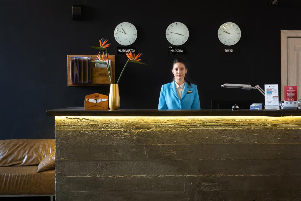 a man standing behind a counter with clocks on the wall at Astoria Hotel in Vladivostok