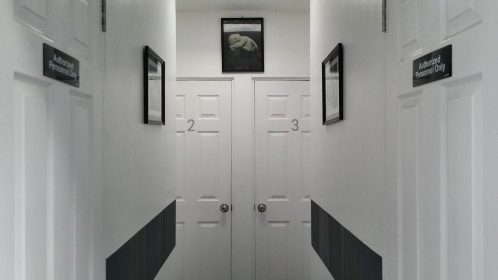 a hallway with white doors and pictures on the walls at ERVORUTO HOSTEL 23 Makati in Manila