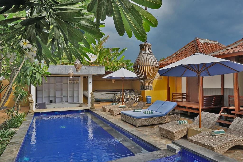 a pool with chairs and umbrellas next to a house at Sari Gili Bungalow in Gili Air