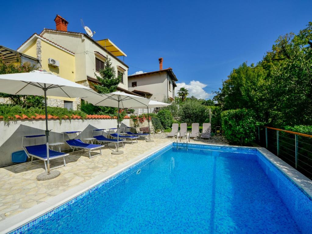 a swimming pool with chairs and umbrellas next to a house at Apartment Lucija by Interhome in Matulji