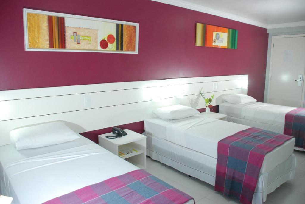 a room with three beds and a red wall at Veleiros Mar Hotel in São Luís