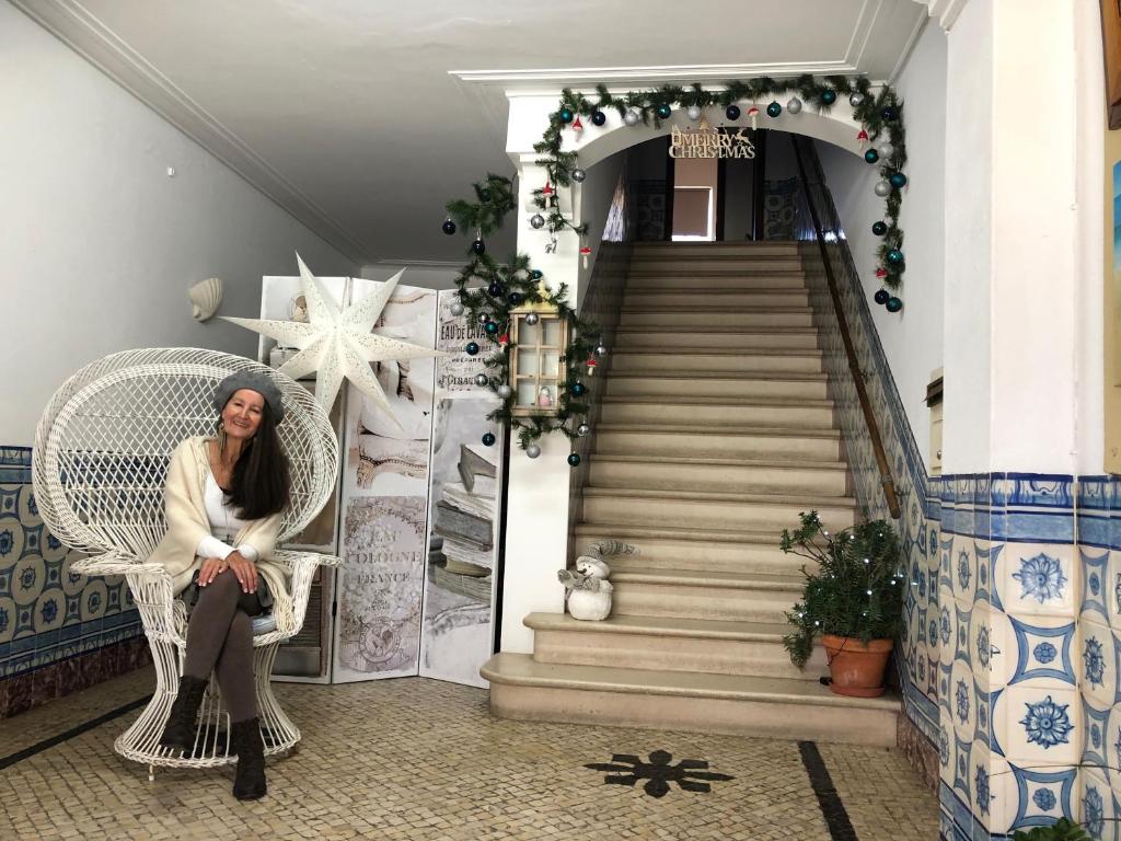 une femme assise dans une chaise en osier à côté d'un escalier dans l'établissement Maria Guest house, à Albufeira