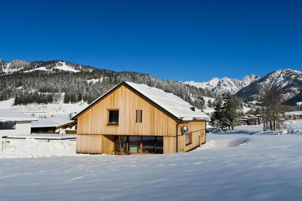 a wooden house in the snow with mountains in the background at Appartement Hochsitz in Hochfilzen