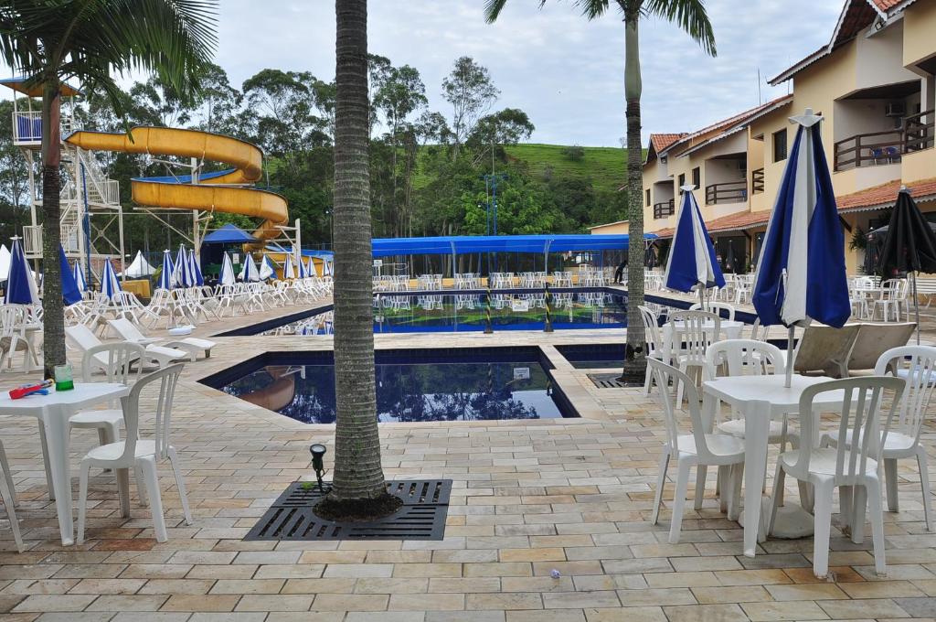 uma piscina com mesas e cadeiras brancas e um escorrega em Resort Recanto do Teixeira All Inclusive em Nazaré Paulista