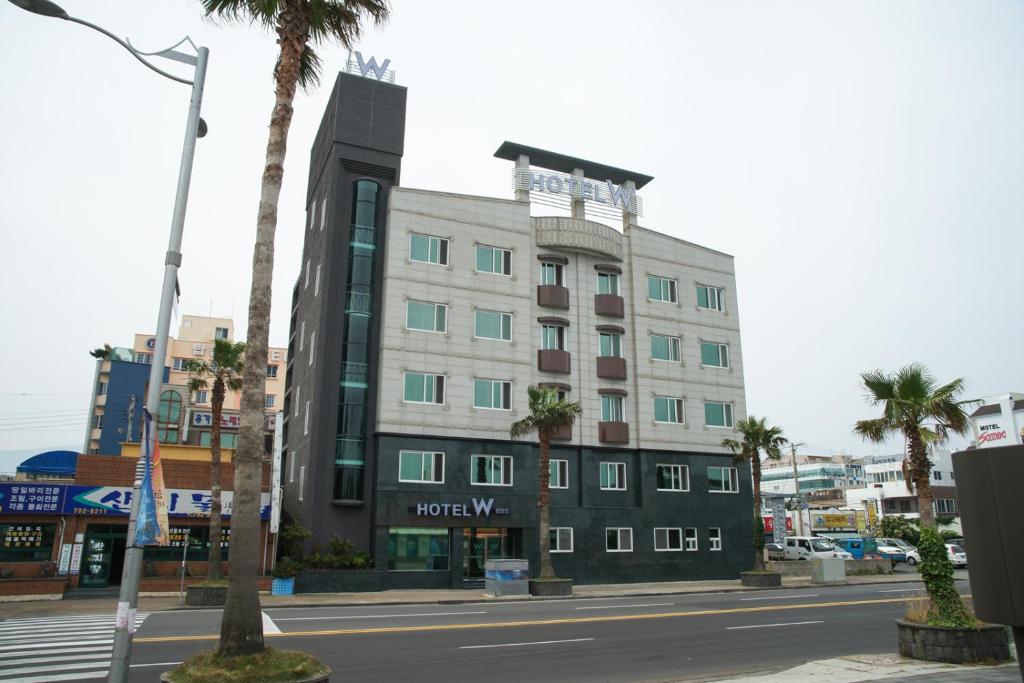a hotel on a city street with a palm tree at Hotel W Topdong in Jeju