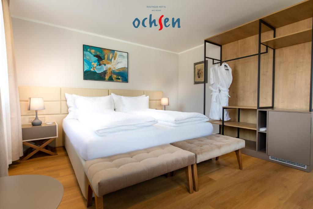 a bedroom with a large white bed with a bench at Boutique Hotel OchSen in Bad Ragaz