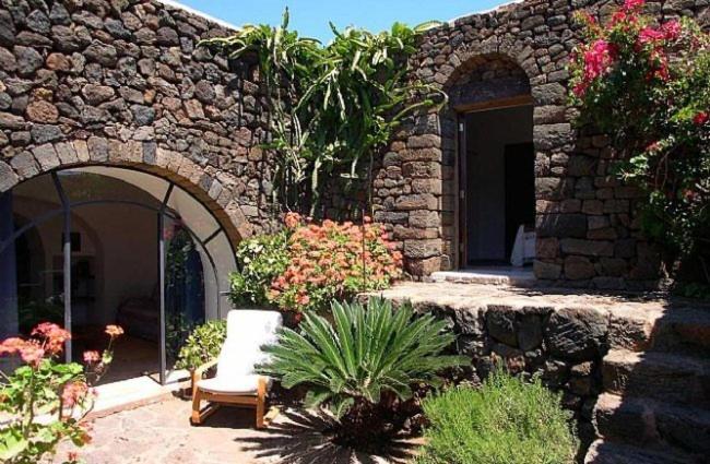 a stone building with a chair and some flowers at Dammuso Sant'Anna in Pantelleria